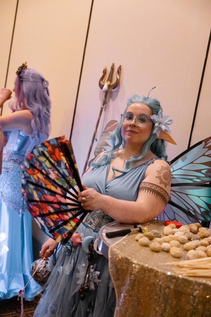 A guest in blue fairy wings holding a colorful fan at Phantoms of the Deep